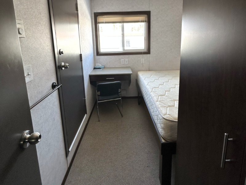 Modular camp bedroom with carpet flooring with a bed and a small desk