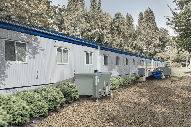 prefabricated dorm modular surrounded by trees with a gravel foreground