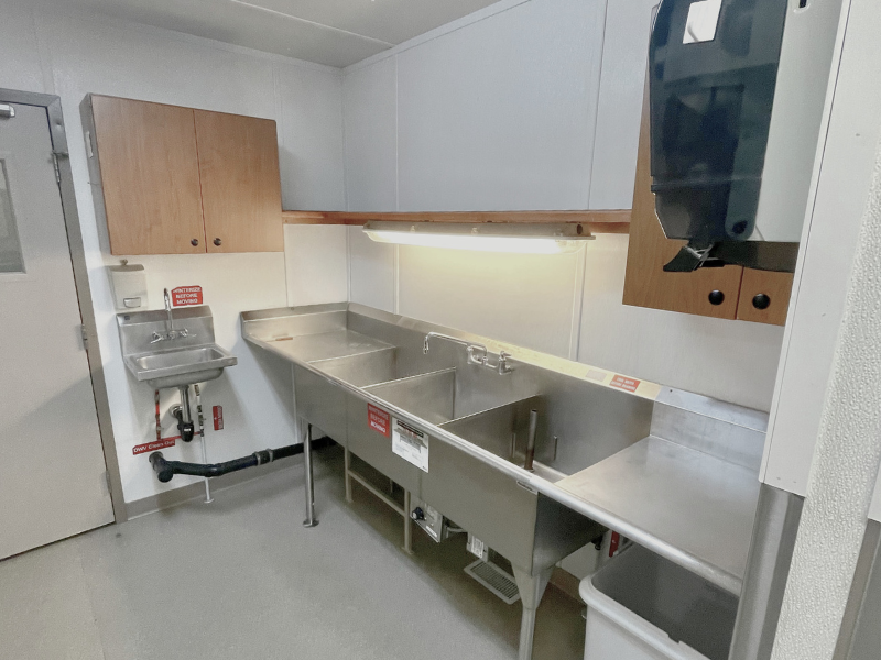 Commercial camp modular kitchen washing station with white walls and grey flooring